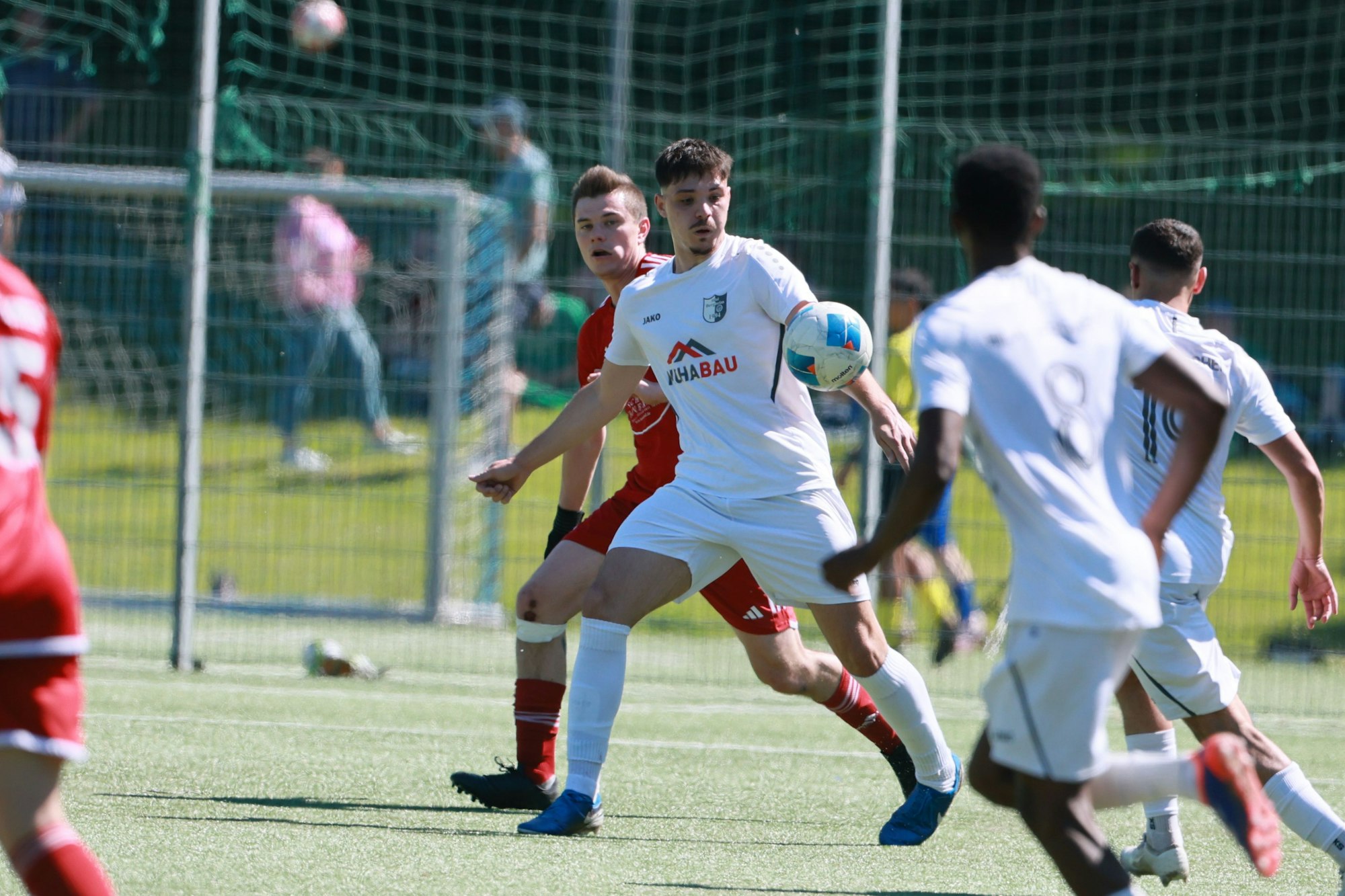 Das Foto zeigt einen Fußballer im weißen Trikot, der vor seinem Gegenspieler den Ball mit der Brust annimmmt.