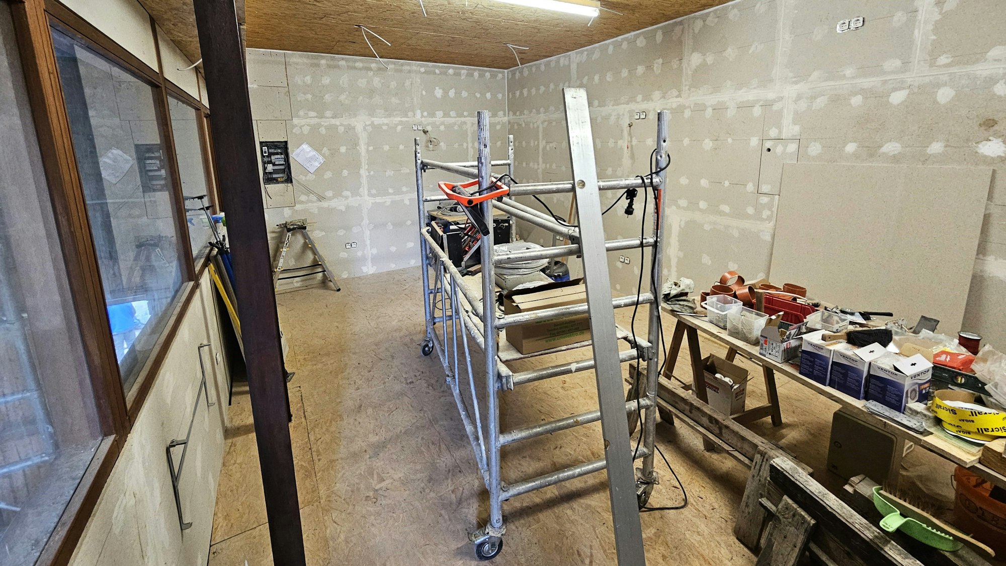 Die Dorfscheune ist derzeit eine Baustelle: Werkzeuge, Baumaterial und ein fahrbares Gerüst stehen in einem Innenraum.