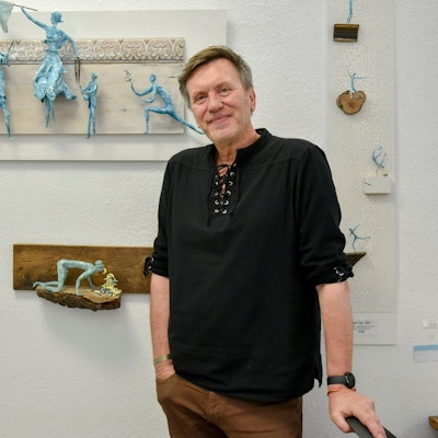 Andre Duront steht vor seinen Skulptren, die dank Magneten an der Wand hängen.