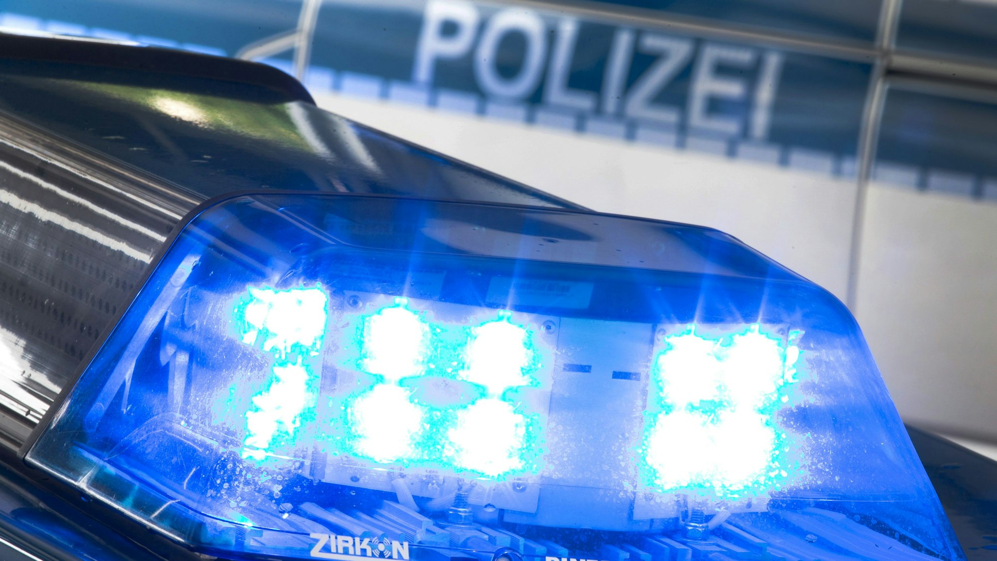 Eine Blaulicht leuchtet auf dem Dach eines Polizeiwagens. Im Hintergrund steht ein weiterer Streifenwagen.
