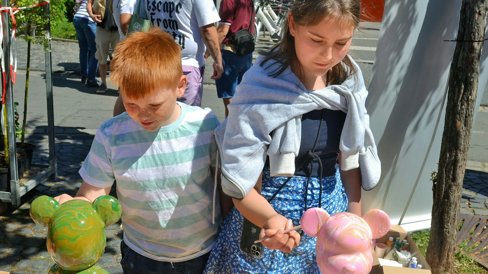 Ein Junge und ein Mädchen stehen vor zwei Bärenskulpturen, die sie mit mit Pinseln anmalen.