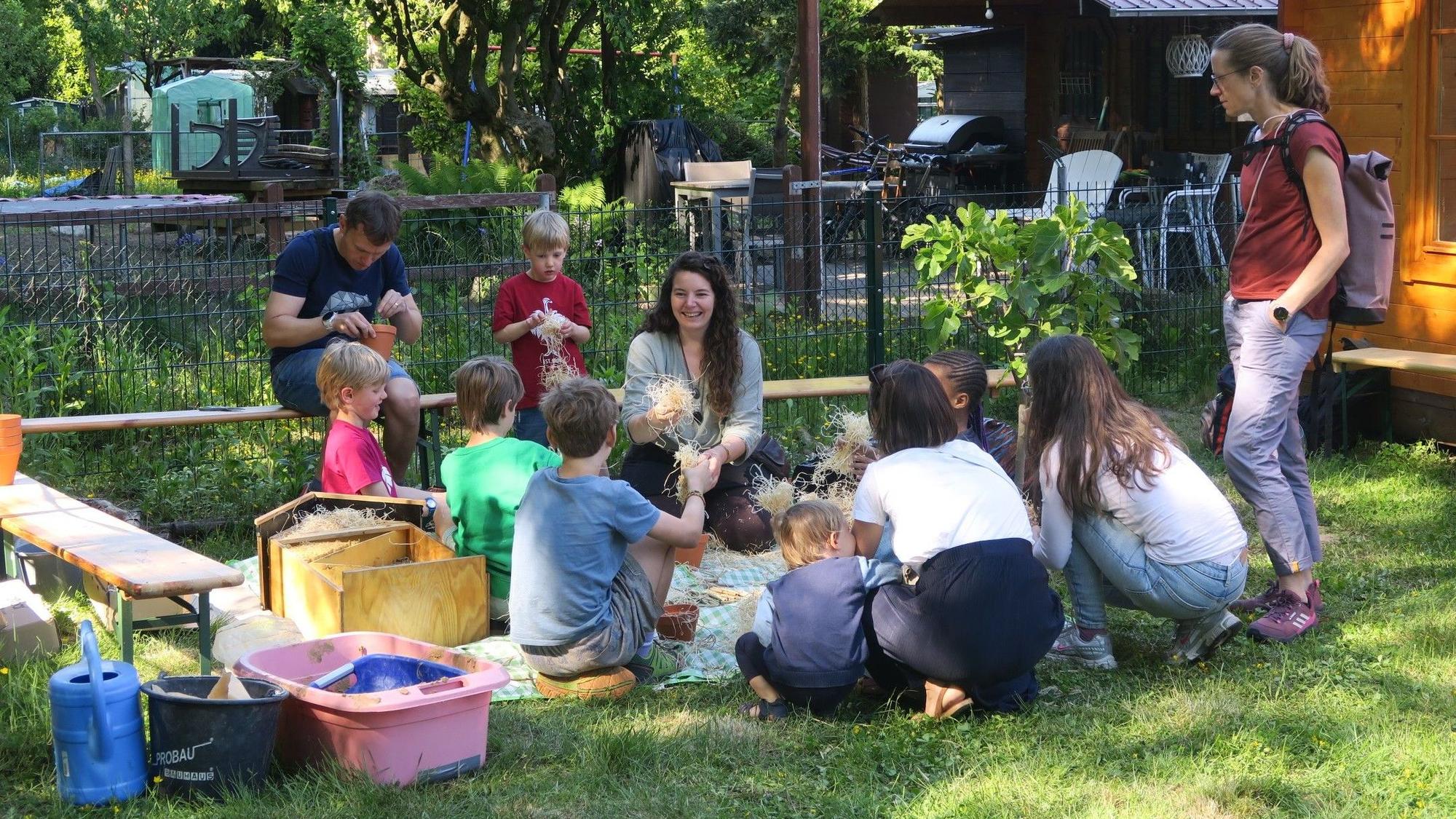 Eine Frau (Mitte, knieend) leitet Kinder beim Basteln von Nistplätzen für Ohrenkneifer an.