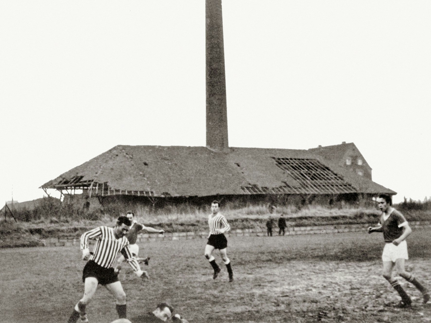 Vor dem verfallenden Gebäude einer Ziegelei spielen Männer Fußball.