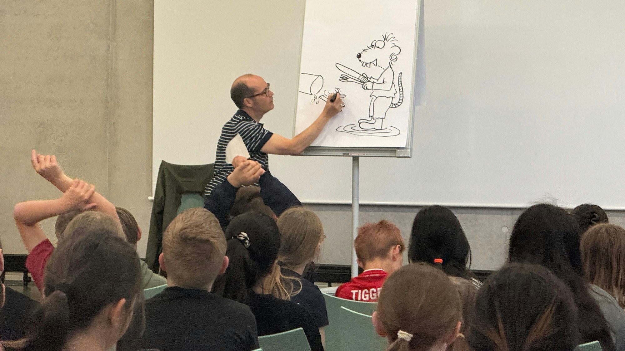 Ein Mann zeichnet vor Kindern eine Zeichentrickfigur auf ein großes Blatt Papier.