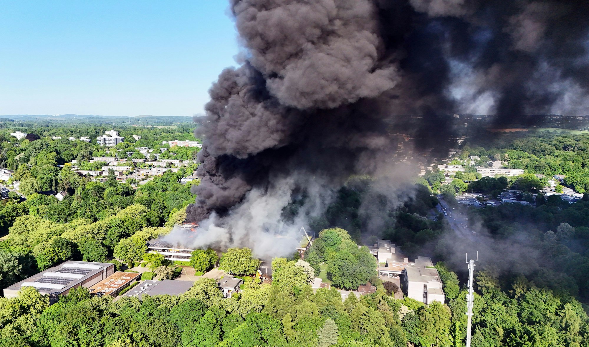13.05.2025, Nordrhein-Westfalen, Erkrath: Eine schwarze Rauchwolke ist bei einem Großbrand über einem Gebäudekomplex mit mehreren Schulen im Kreis Mettmann zu sehen. Das Feuer sei am Nachmittag ausgebrochen, sagte eine Sprecherin der Polizei. Schülerinnen und Schüler seien zu dem Zeitpunkt nicht mehr vor Ort gewesen. (Luftaufnahme mit einer Drohne) Foto: Gianni Gattus/dpa +++ dpa-Bildfunk +++