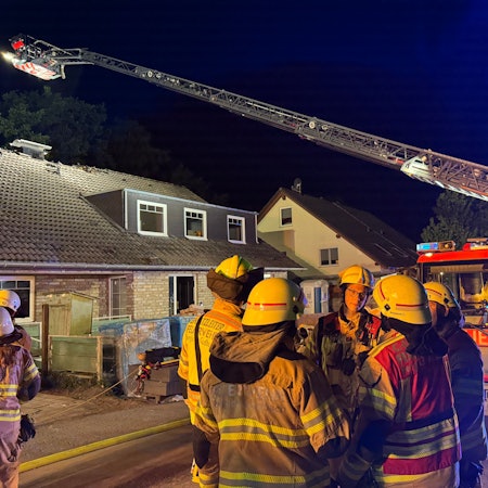 Eine Drehleiter der Feuerwehr Bergisch Gladbach steht an einem Haus im Alten Traßweg in Bergisch Gladbach-Kippekausen. Feuerwehrleute stehen davor.