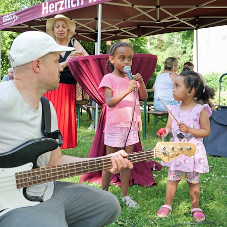 Ein Mann spielt Gitarre, zwei Mädchen singen und musizieren dazu.