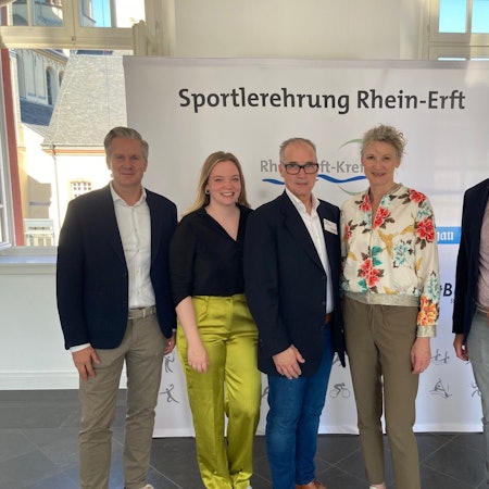 Männer und Frauen stehen vor einem Banner, auf dem „Sportlerehrung Rhein-Erft“ steht.