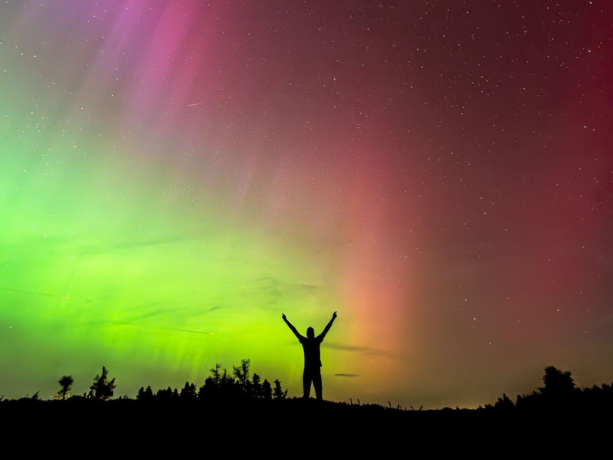 Ein Mann reckt unter Polarlichtern am Himmel die Arme in die Höhe.