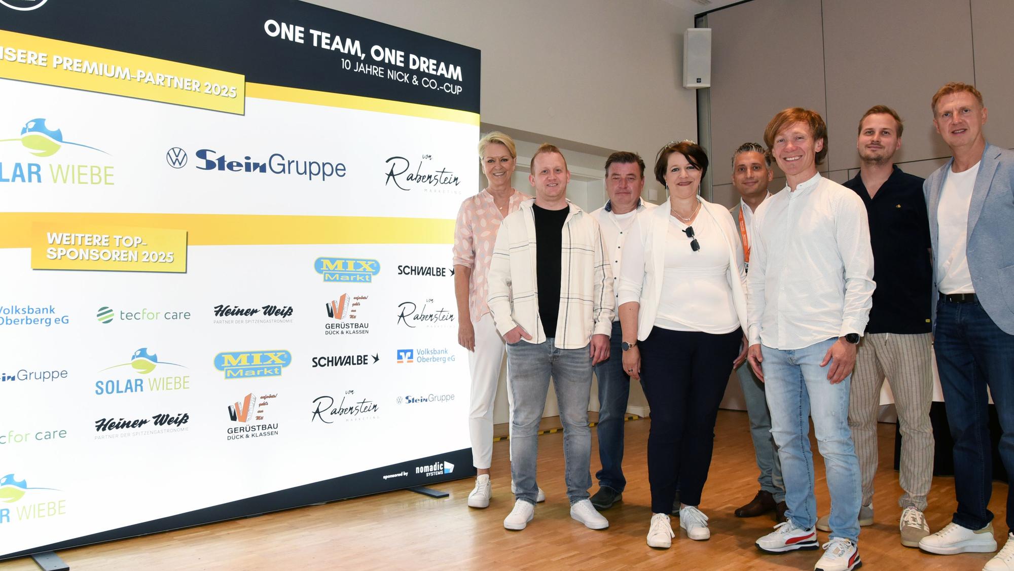 Initiatoren und Sponsoren präsentieren sich vor der Sponsorenwand des Nick & Co.-Cups.