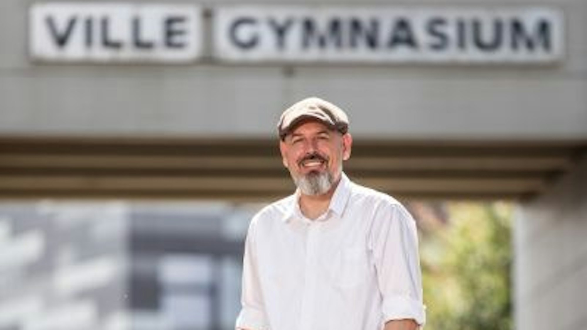 Auf dem Foto ist ein Mann mit Vollbart in weißem Hemd und einer Schiebermütze zu sehen.