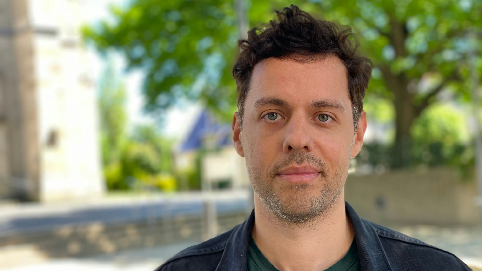 Ein Porträt von Stephan Hellweg. Im Hintergrund ist verschwommen die Herz-Jesu-Kirche zu sehen.