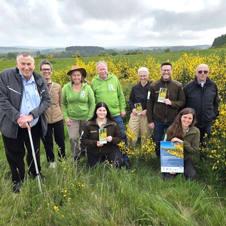 Vertreterinnen und Vertreter der beteiligten Organisationen haben sich neben blühenden Ginsterbüschen zum Gruppenbild aufgestellt.
