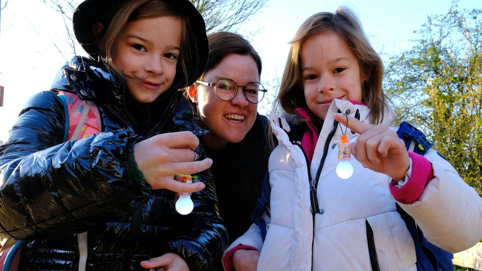 Die beiden Mädchen zeigen ein kleines LED-Lämpchen, die Mutter der Kinder steht zwischen den beiden.