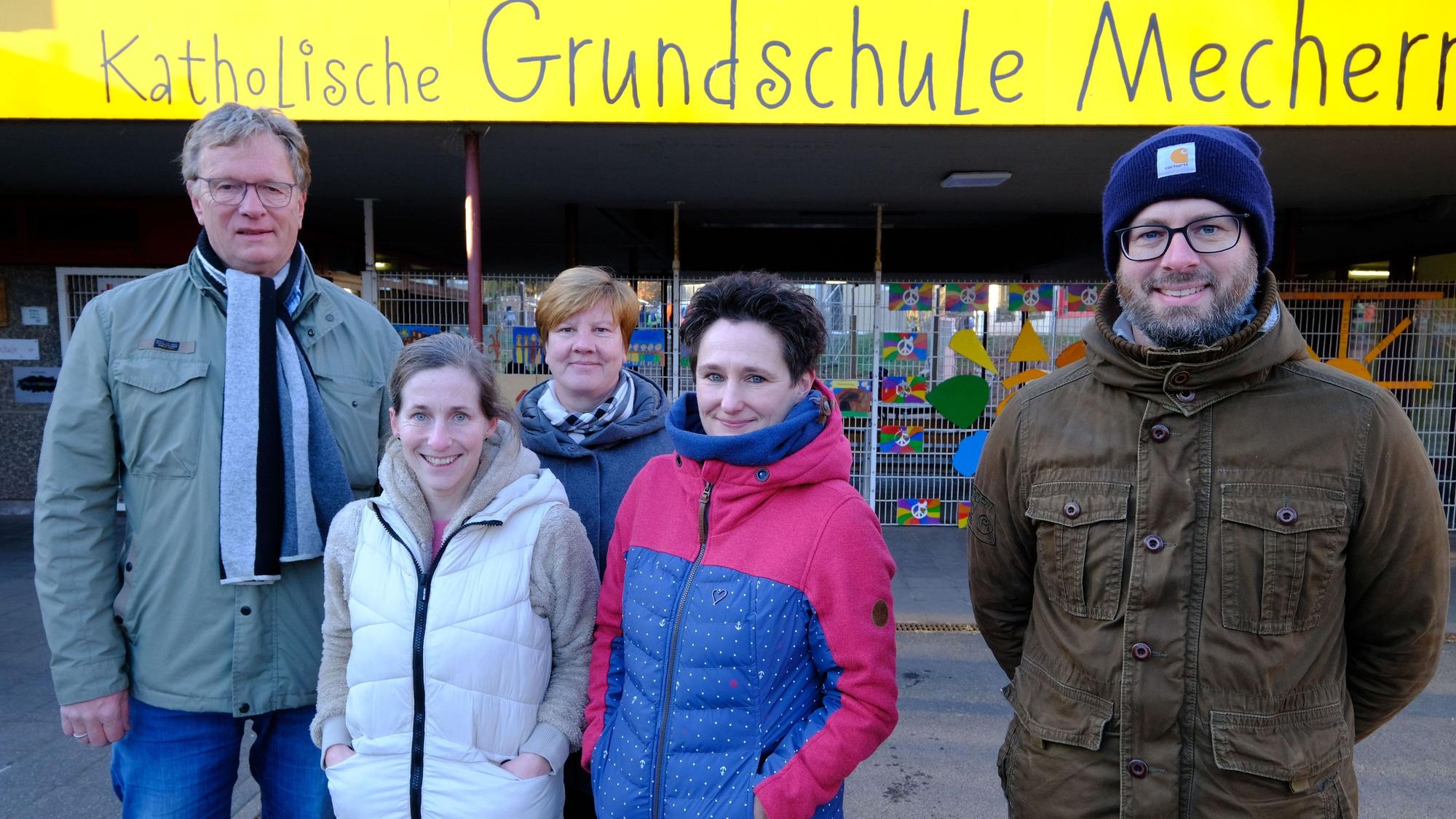 Die drei Frauen und zwei Männer stehen unter einem Schild mit der Aufschrift „Katholische Grundschule Mechernich“.