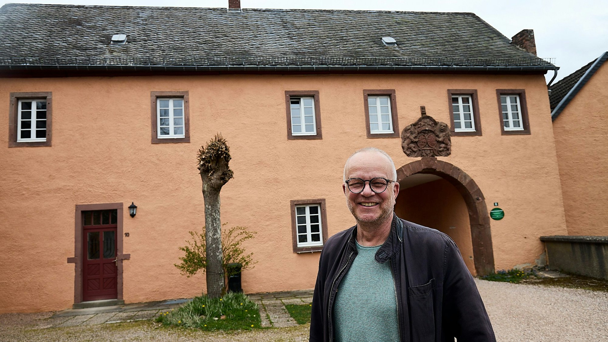 Das Bild zeigt einen Mann, der in die Kamera lacht, hinter ihm ein historisches Gebäude.