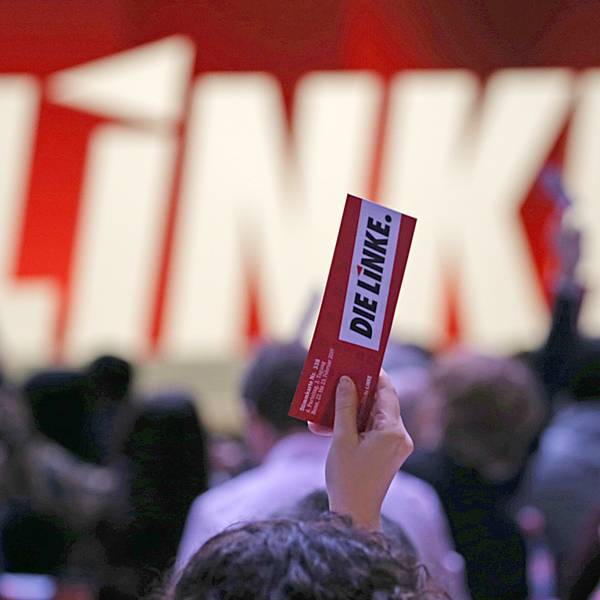 In einer Hand hält jemand, der nicht zu sehen ist, einen Zettel, auf dem „Die Linke“ steht.