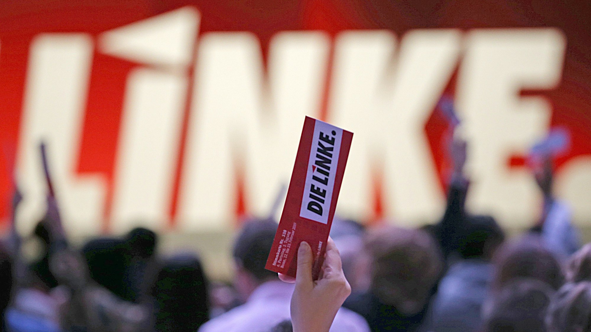 In einer Hand hält jemand, der nicht zu sehen ist, einen Zettel, auf dem „Die Linke“ steht.