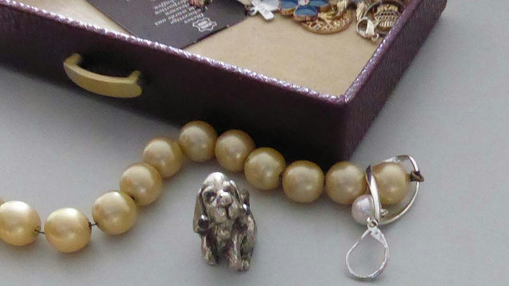 Das Bild zeigt eine Perlenkette und einen Anhänger in Form eines Hundes.