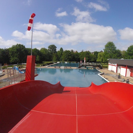 Das Bild zeigt eine rote Rutsche, die in ein Wasserbecken des Freibads führt.