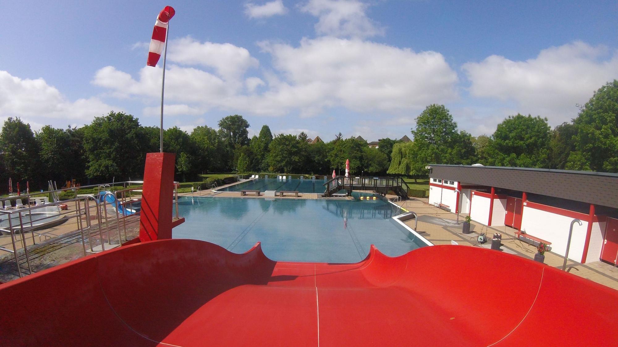 Das Bild zeigt eine rote Rutsche, die in ein Wasserbecken des Freibads führt.