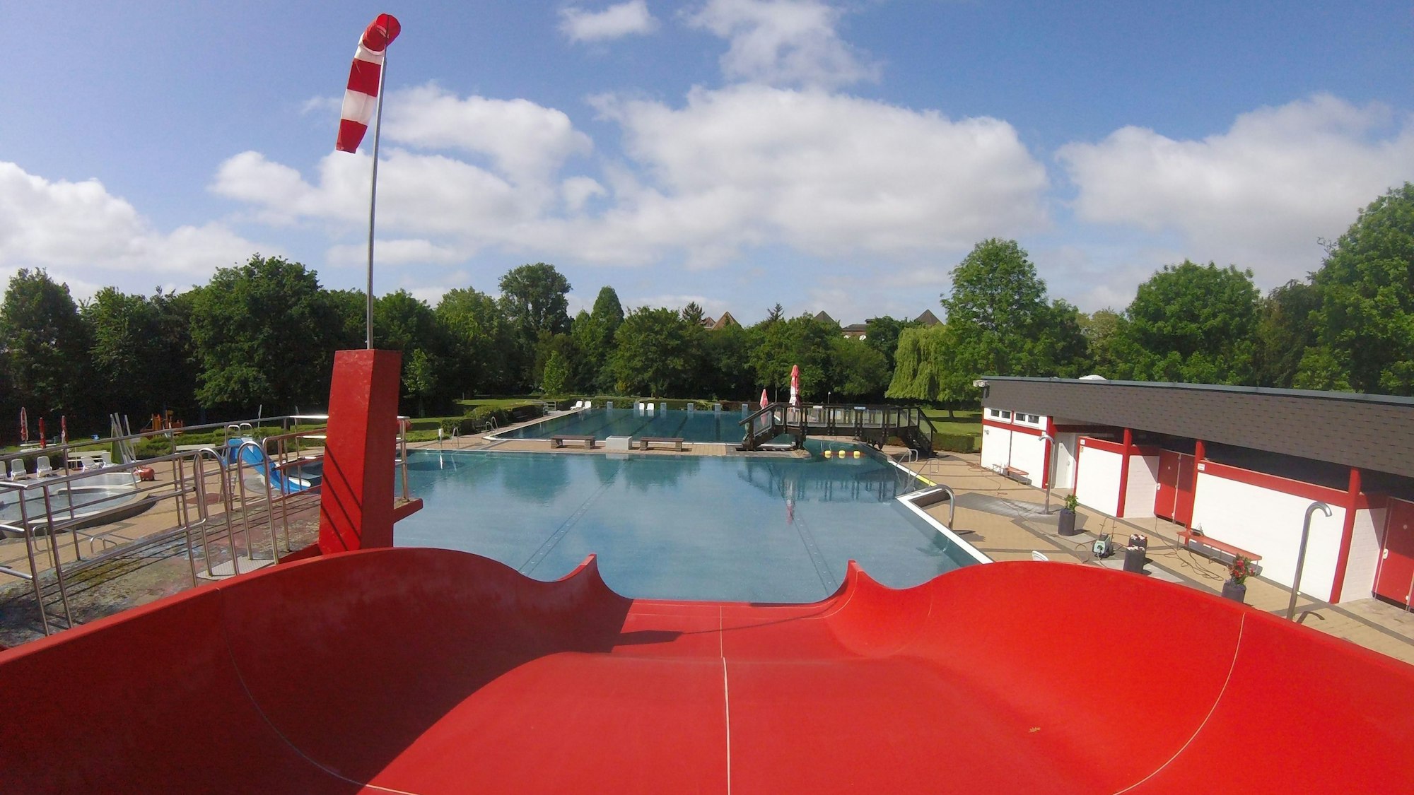 Das Bild zeigt eine rote Rutsche, die in ein Wasserbecken des Freibads führt.