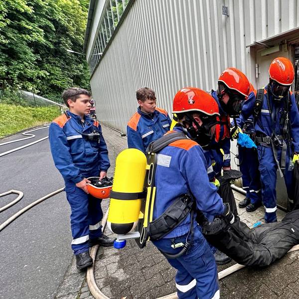 Junge Feuerwehrleute in Atemschutz und Sicherheitshelm tragen einen Dummy aus der Gefahrenzone.