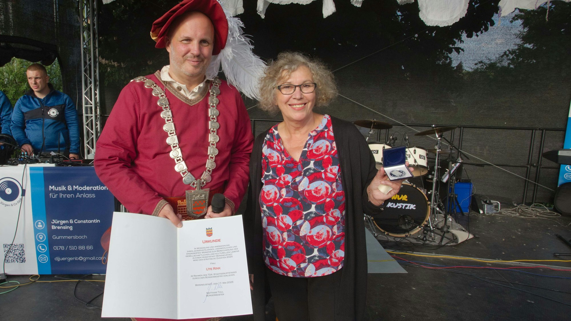 Ein Mann zeigt eine Urkunde, eine Frau eine Medaille.