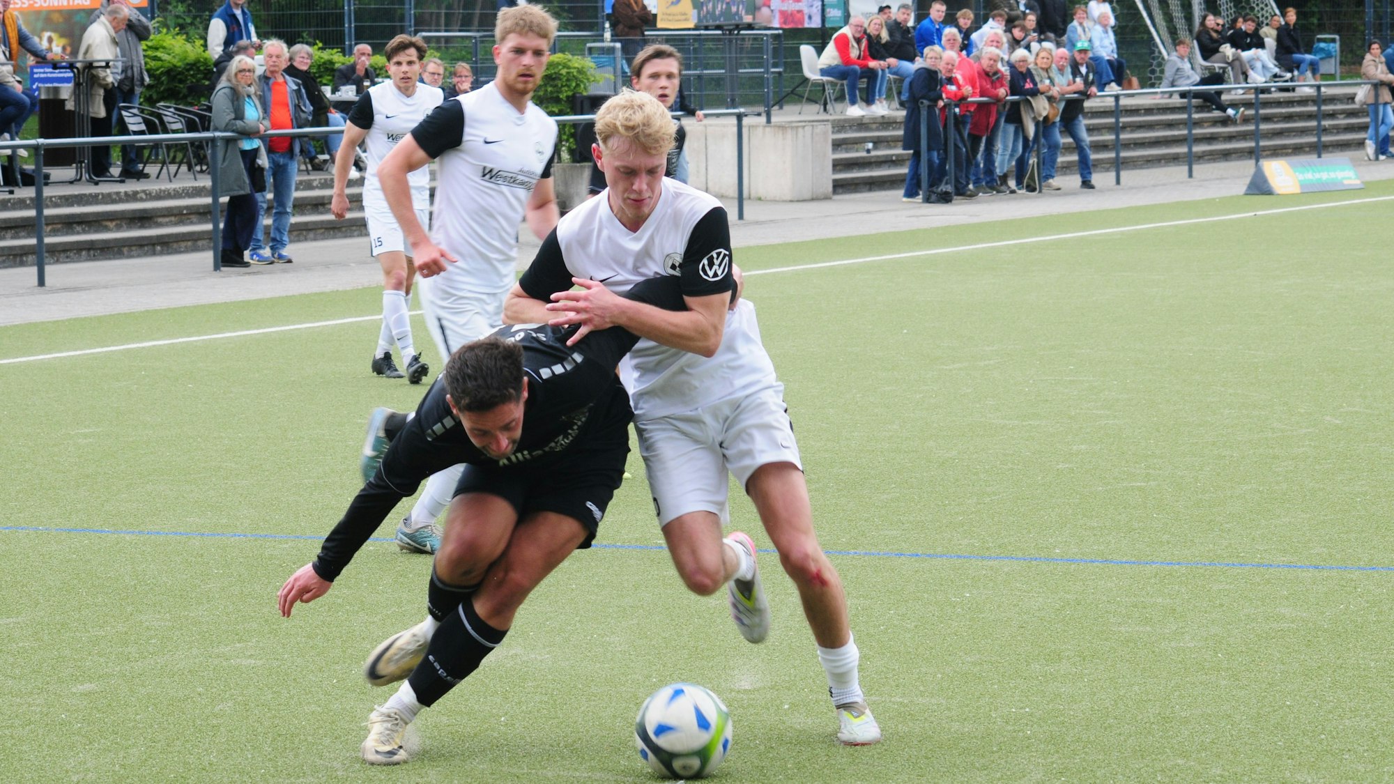 Das Foto zeigt zwei Fußballer im Kampf um den Ball, die sich mit den Armen beharken.