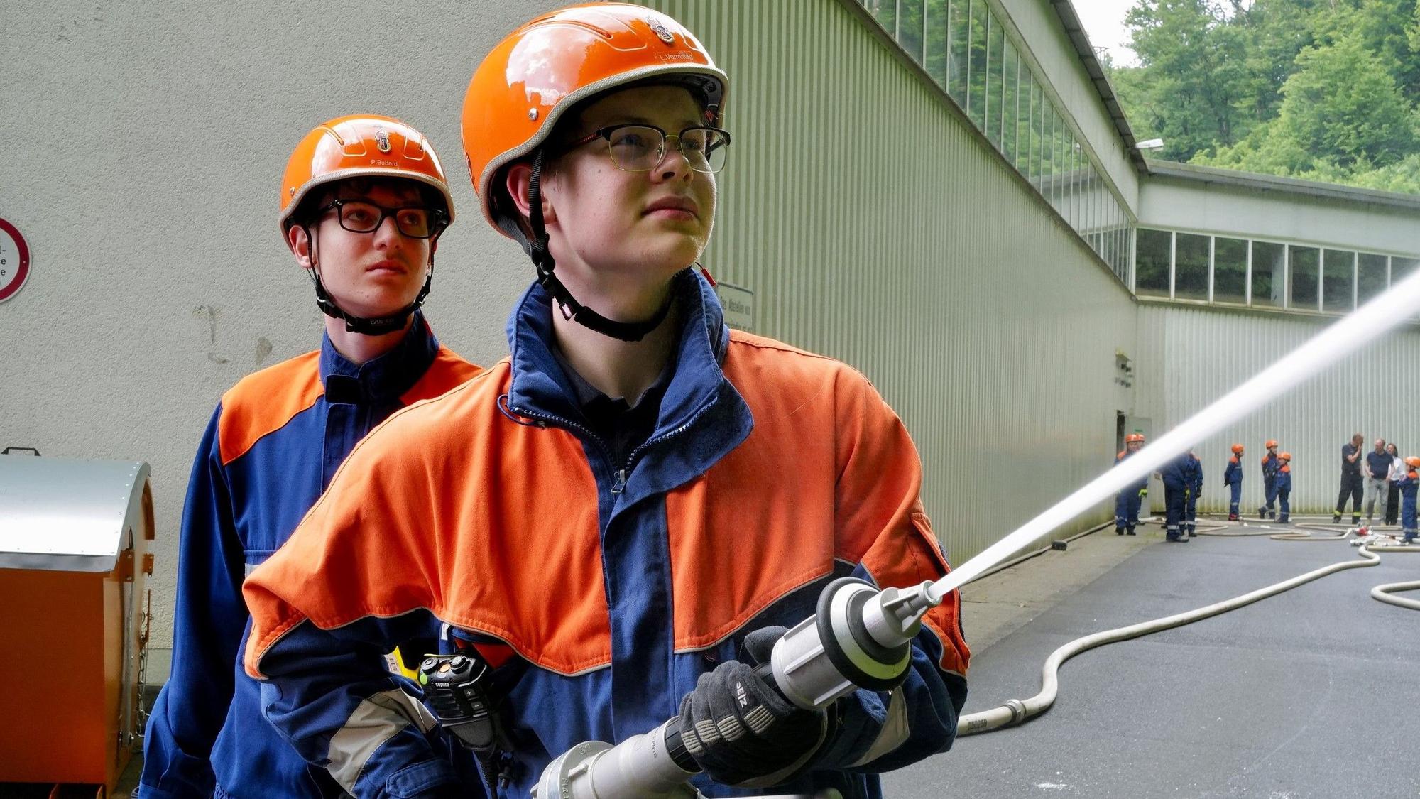 Zwei Jungfeuerwehrleute arbeiten bei der Übung mit einem Wasserschlauch.