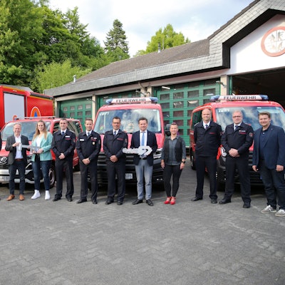 Eine Gruppe steht vor vier Feuerwehrfahrzeugen.