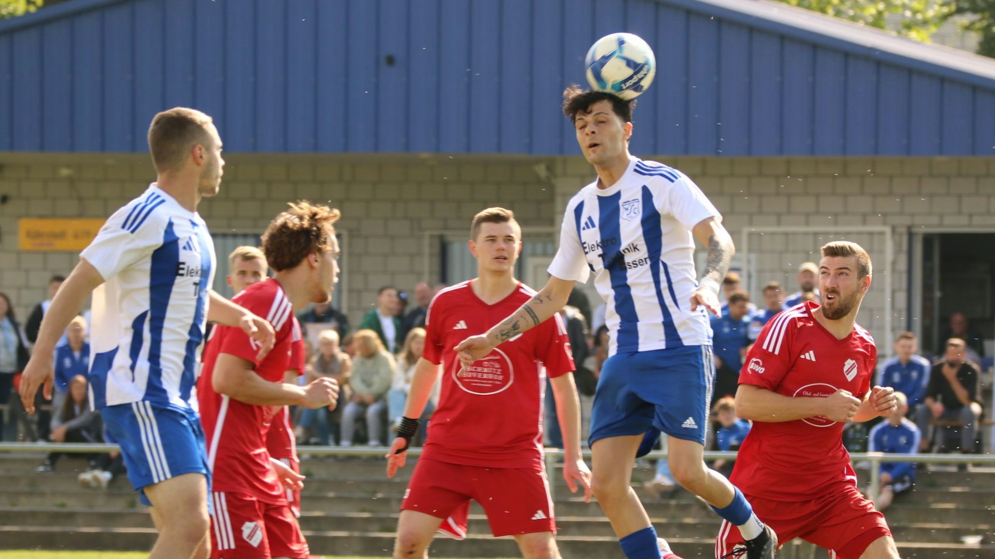 Das Bild zeigt einen Fußballer, der den Ball mit dem Kopf spielt. Mehrere Gegenspieler schauen zu.