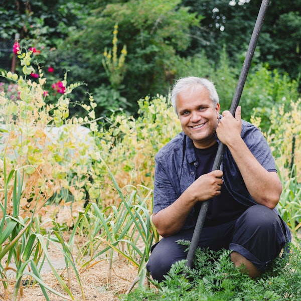 Auf dem Bild ist ein Mann zu sehen, der in seinem Garten auf der Erde hockt.