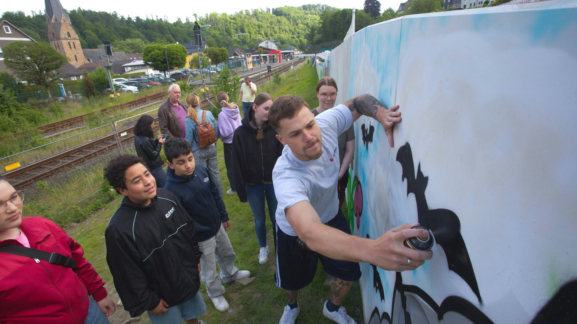 Das Foto zeigt einen Sprayer an einer Mauer und jugendliche Zuschauer.