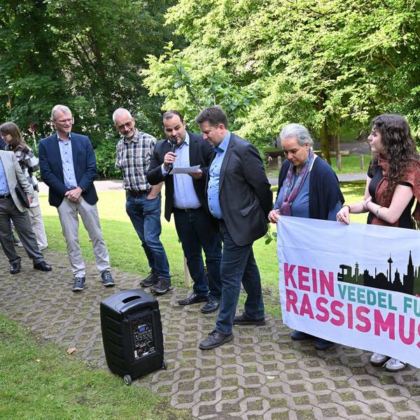 Beteiligte der Veranstaltung halten ein Anti-Rassismus-Plakat in der Hand.