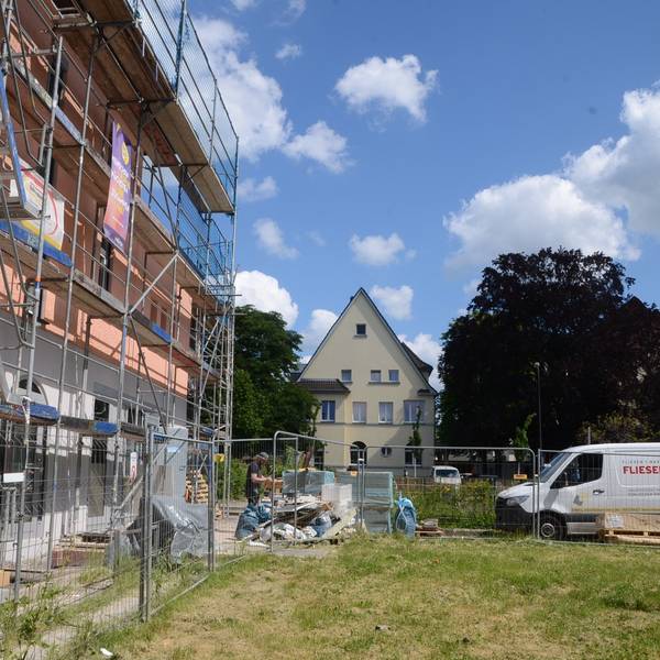 Ein eingerüstetes Gebäude, eine Rasenfläche und ein Kirchturm.
