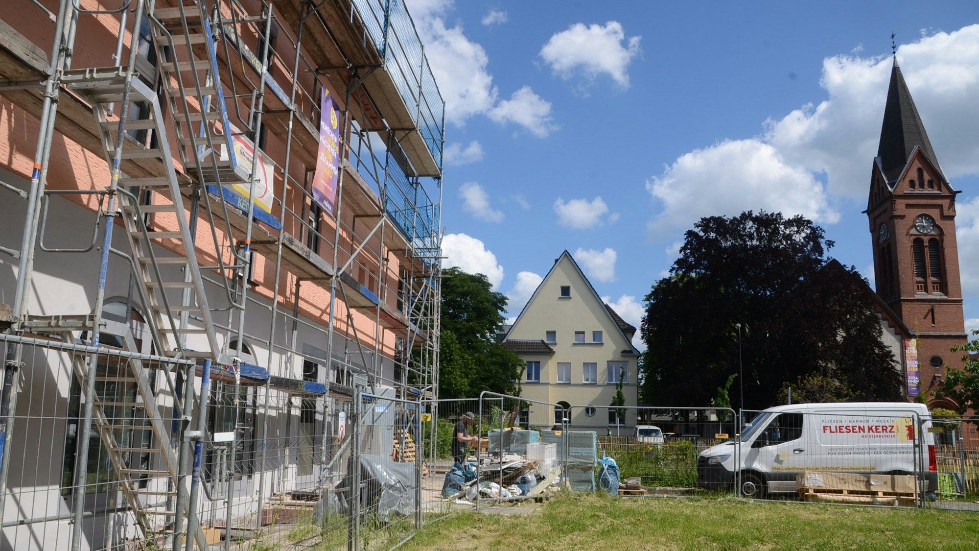Ein eingerüstetes Gebäude, eine Rasenfläche und ein Kirchturm.