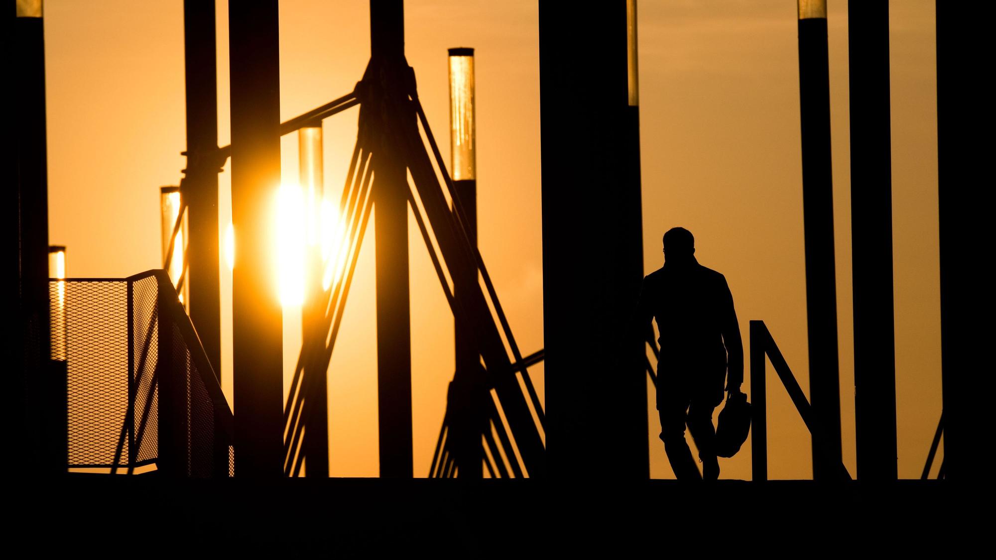 09.04.2019, Niedersachsen, Hannover: Ein Mann geht mit einer Aktentasche bei Sonnenaufgang über eine Brücke an der Expo Plaza.