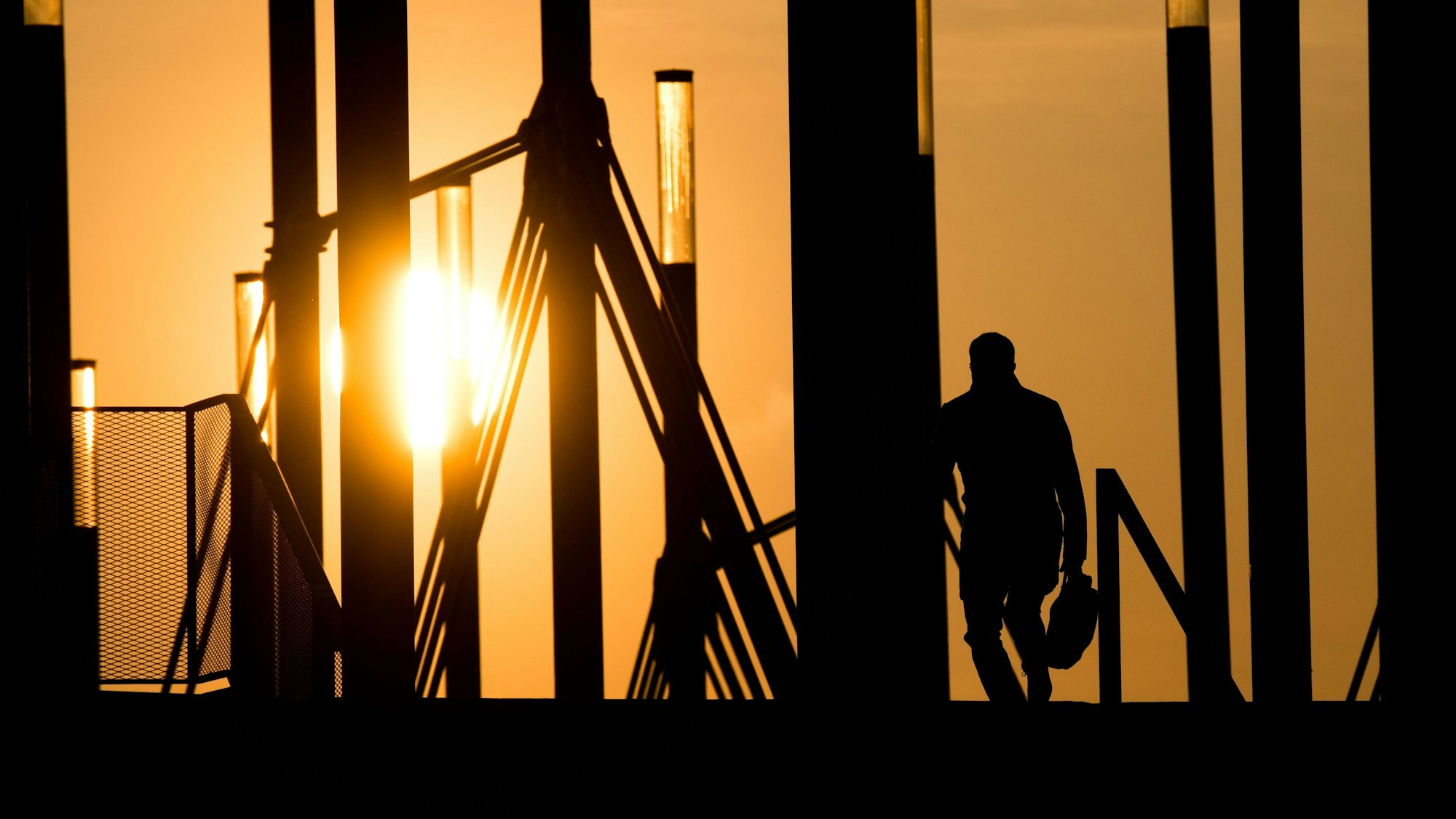 09.04.2019, Niedersachsen, Hannover: Ein Mann geht mit einer Aktentasche bei Sonnenaufgang über eine Brücke an der Expo Plaza.