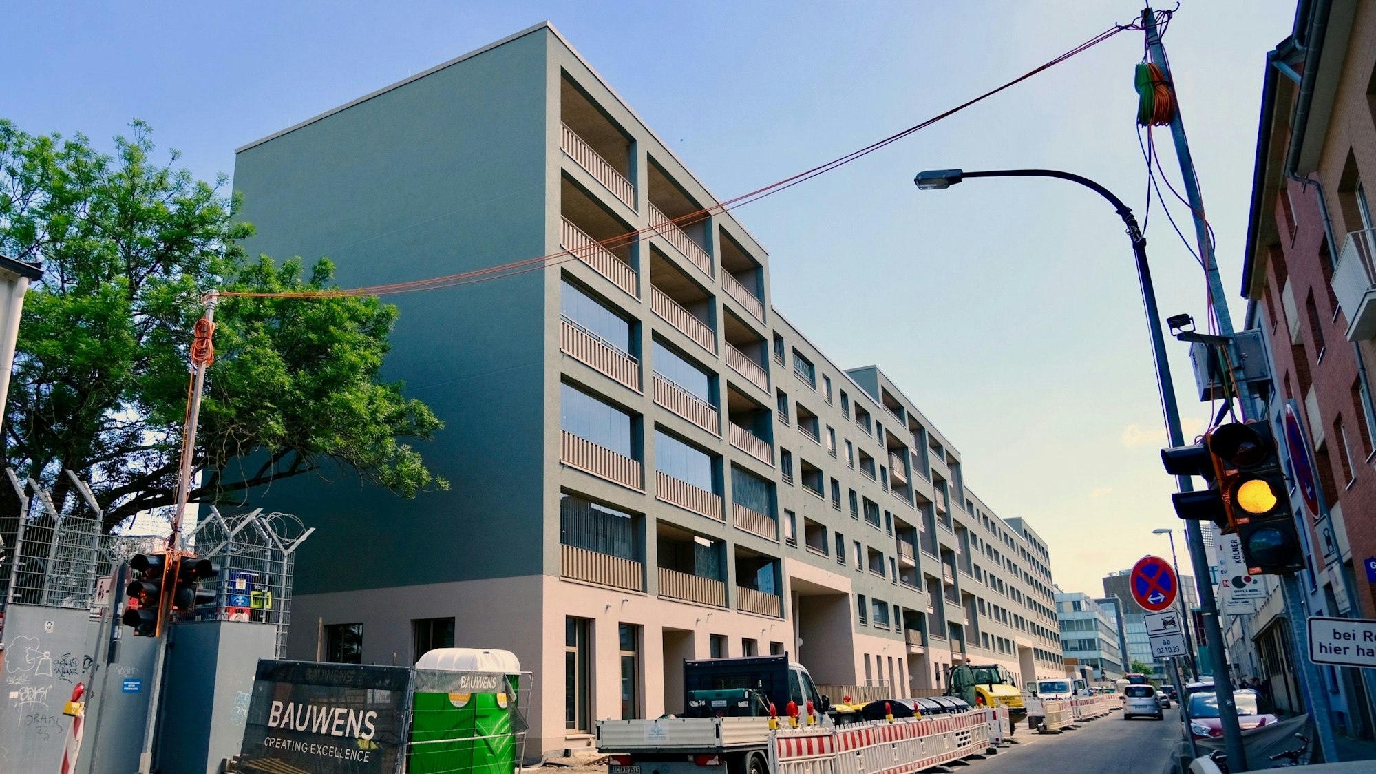 An einer engen Straße steht ein langgezogener Neubau.