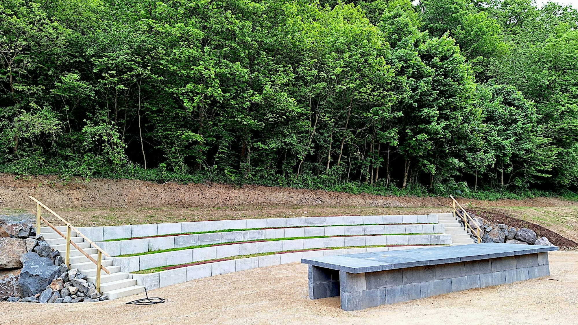 Das Bild zeigt einen Hang, in dem mehrere Reihen Steinstufen eingezogen wurden, davor steht ein langer Tisch aus Stein.
