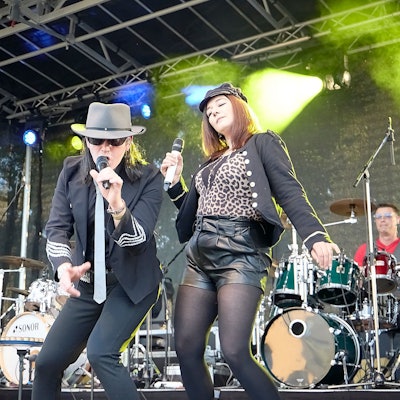 Ein Mann als Udo Lindenberg verkleidet singt in ein Mikrofon, daneben tanzt eine Frau.