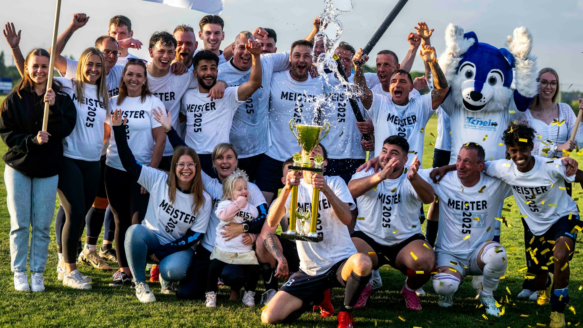 Die SG Ülpenich/Nemmenich/Elsig feiert. Ein Spieler hält einen Pokal in die Höhe. Auch ein Maskottchen und einige Frauen jubeln mit.