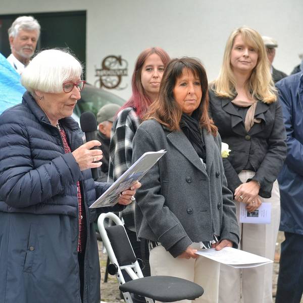 Gisela Freier hält ein Mikrofon und ein Manuskript in den Händen. Daneben stehen einige der Besucher.