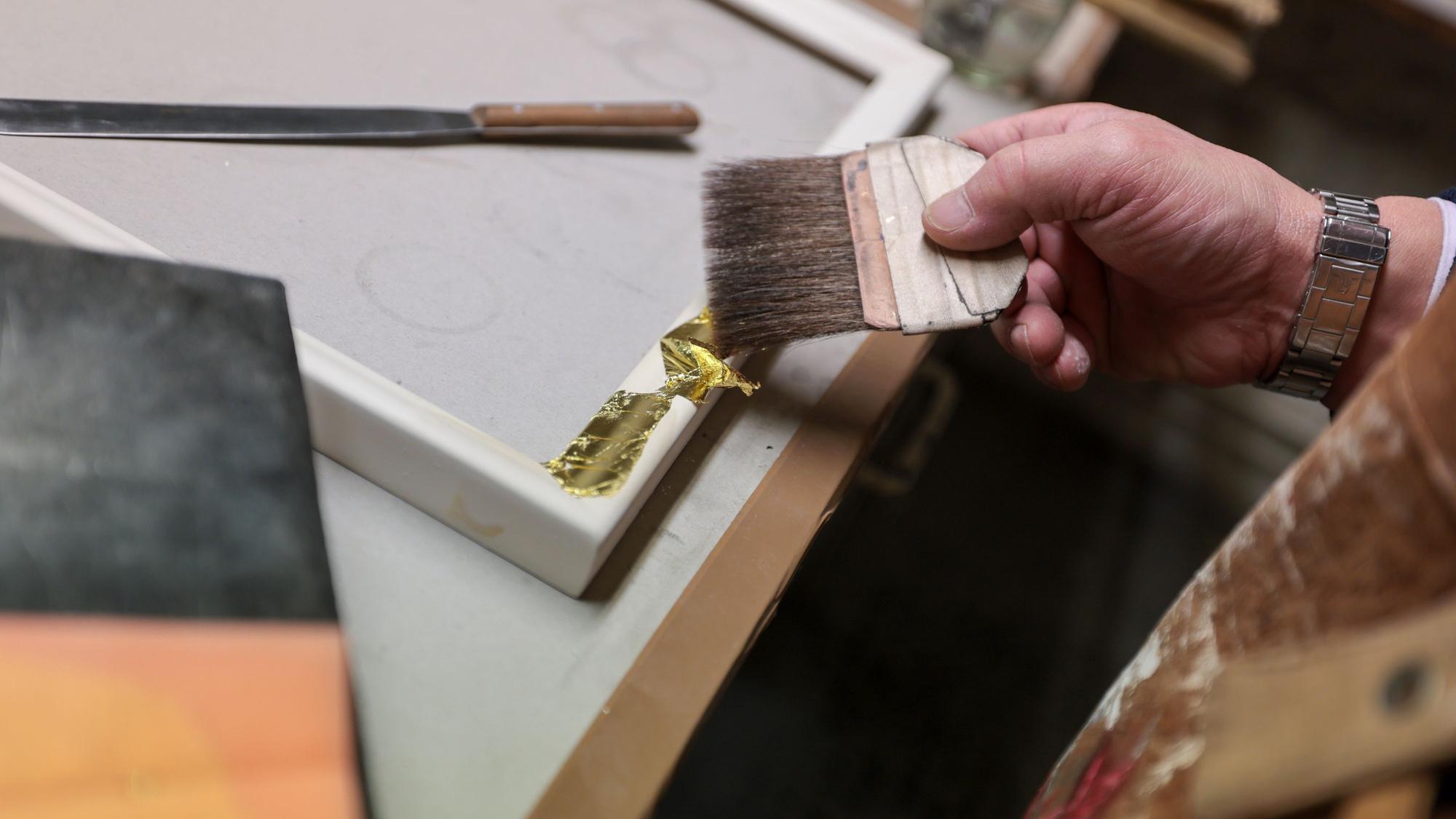 In Handarbeit werden die hauchdünnen Blattgold-Stücke auf die Rahmen aufgetragen.