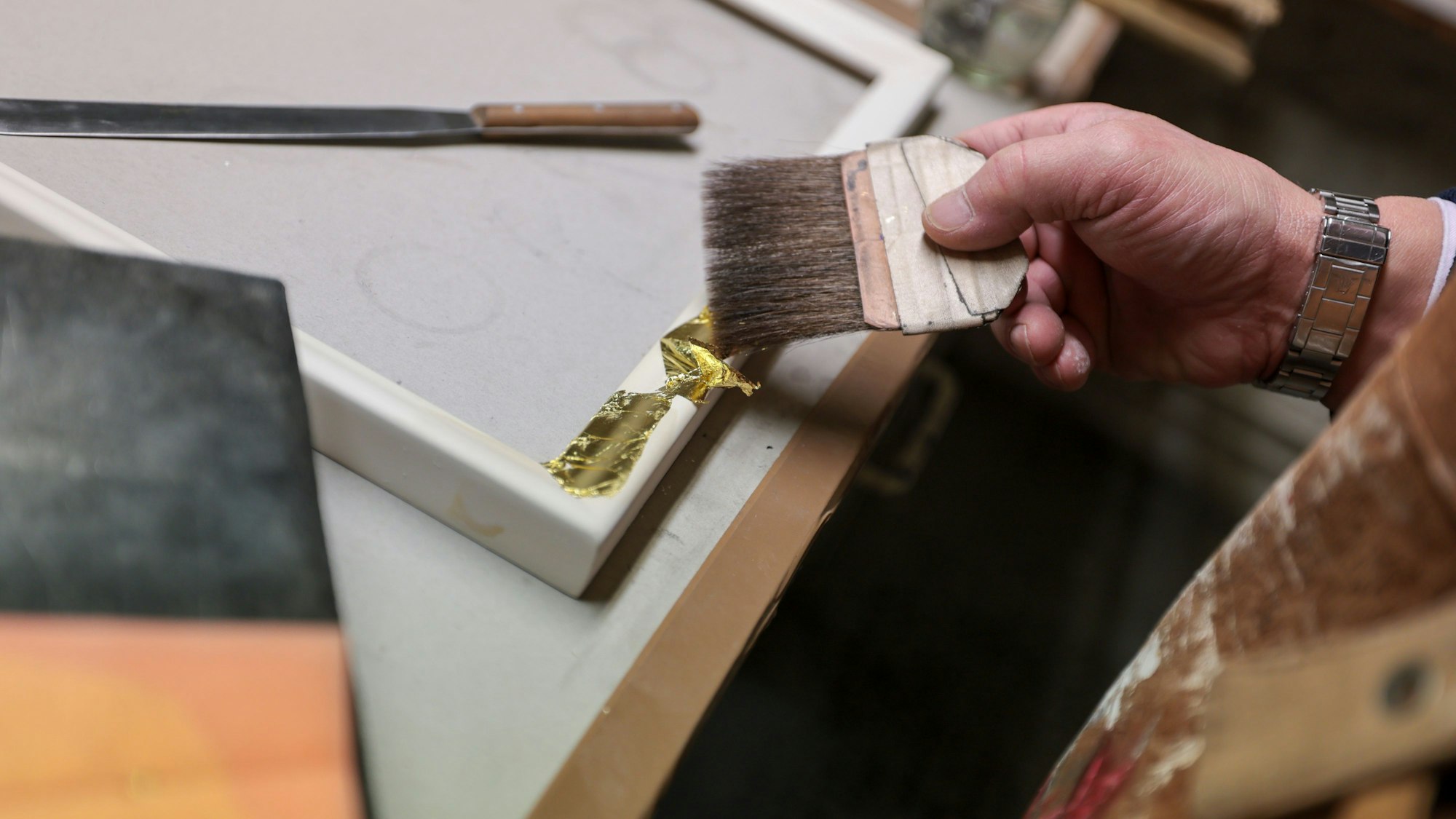 In Handarbeit werden die hauchdünnen Blattgold-Stücke auf die Rahmen aufgetragen.