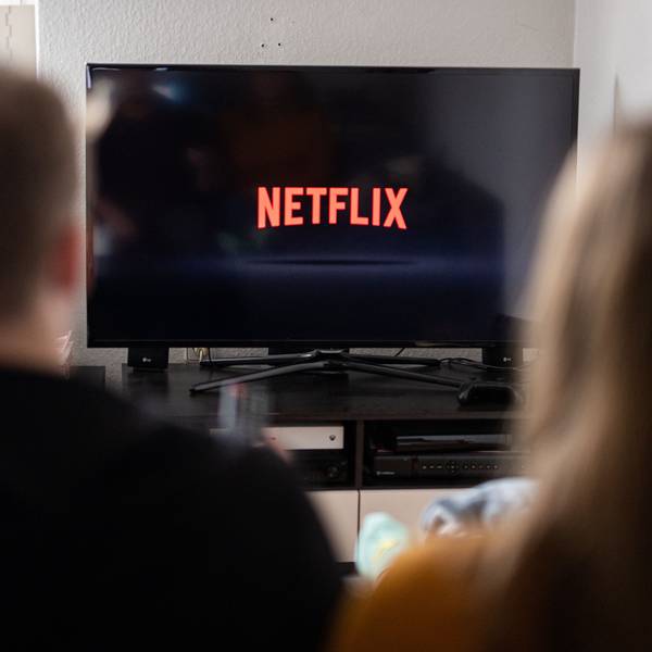 Ein Paar sitzt vor dem Fernseher, auf dem das Netflix-Logo zu sehen ist.