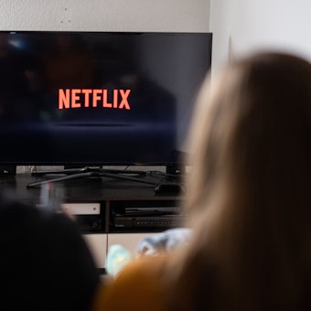 Ein Paar sitzt vor dem Fernseher, auf dem das Netflix-Logo zu sehen ist.