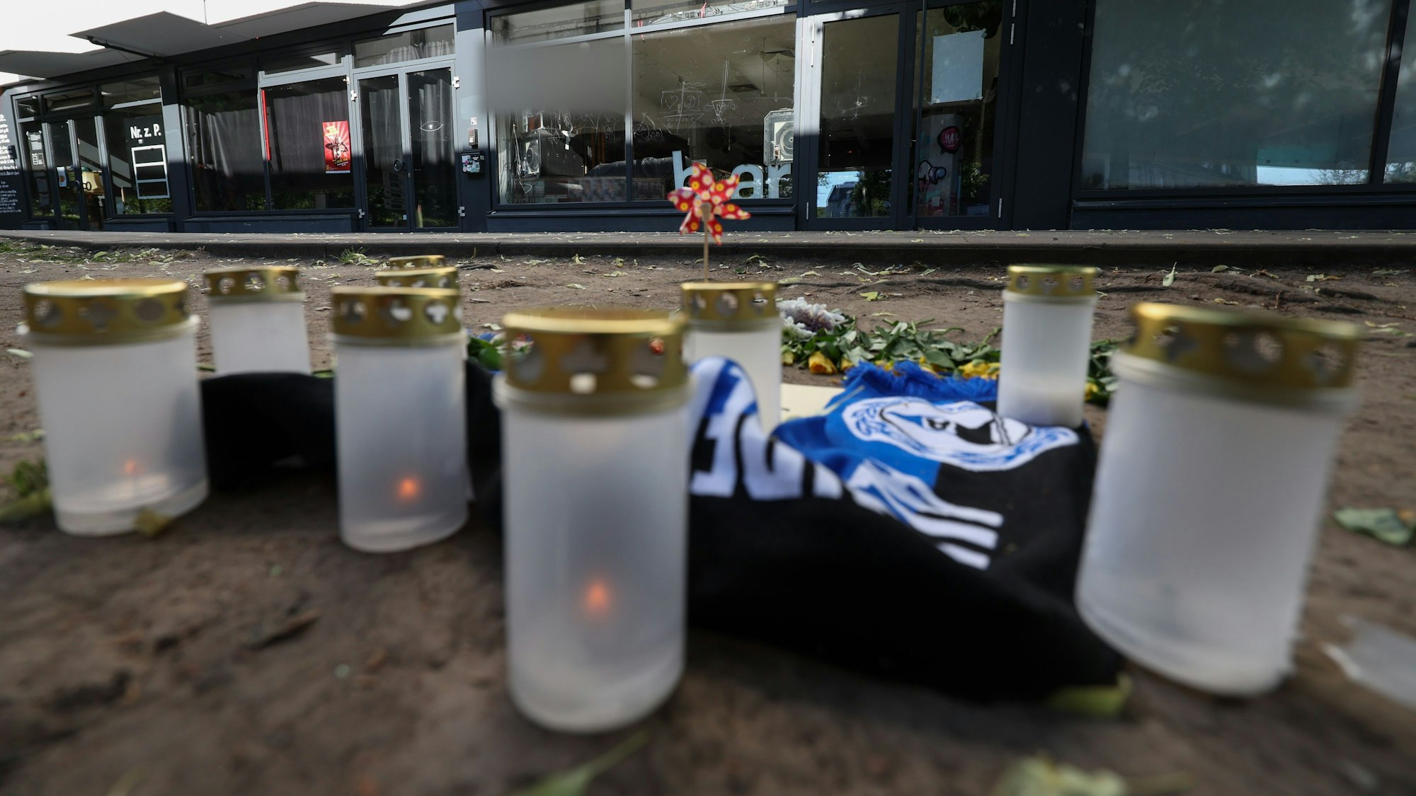 20.05.2025, Nordrhein-Westfalen, Bielefeld: Kerzen und ein Fanschal von Arminia Bielefeld sind an einem Tatort in der Innenstadt zu sehen. Nach dem Angriff eines Mannes auf mindestens fünf Menschen vor einer Bar in Bielefeld ist ein Tatverdächtiger in Untersuchungshaft. Betroffene des Messerangriffs vor einer Bielefelder Bar können bei einer kostenlosen Hotline Hilfe und psychosoziale Beratung bekommen. Wie der Bundesopferbeauftragte Roland Weber mitteilte, sei eine entsprechend kostenfreie Telefonnummer nun freigeschaltet worden. (zu dpa: «Beratungstelefon für Betroffene des Angriffs von Bielefeld») Foto: Friso Gentsch/dpa +++ dpa-Bildfunk +++