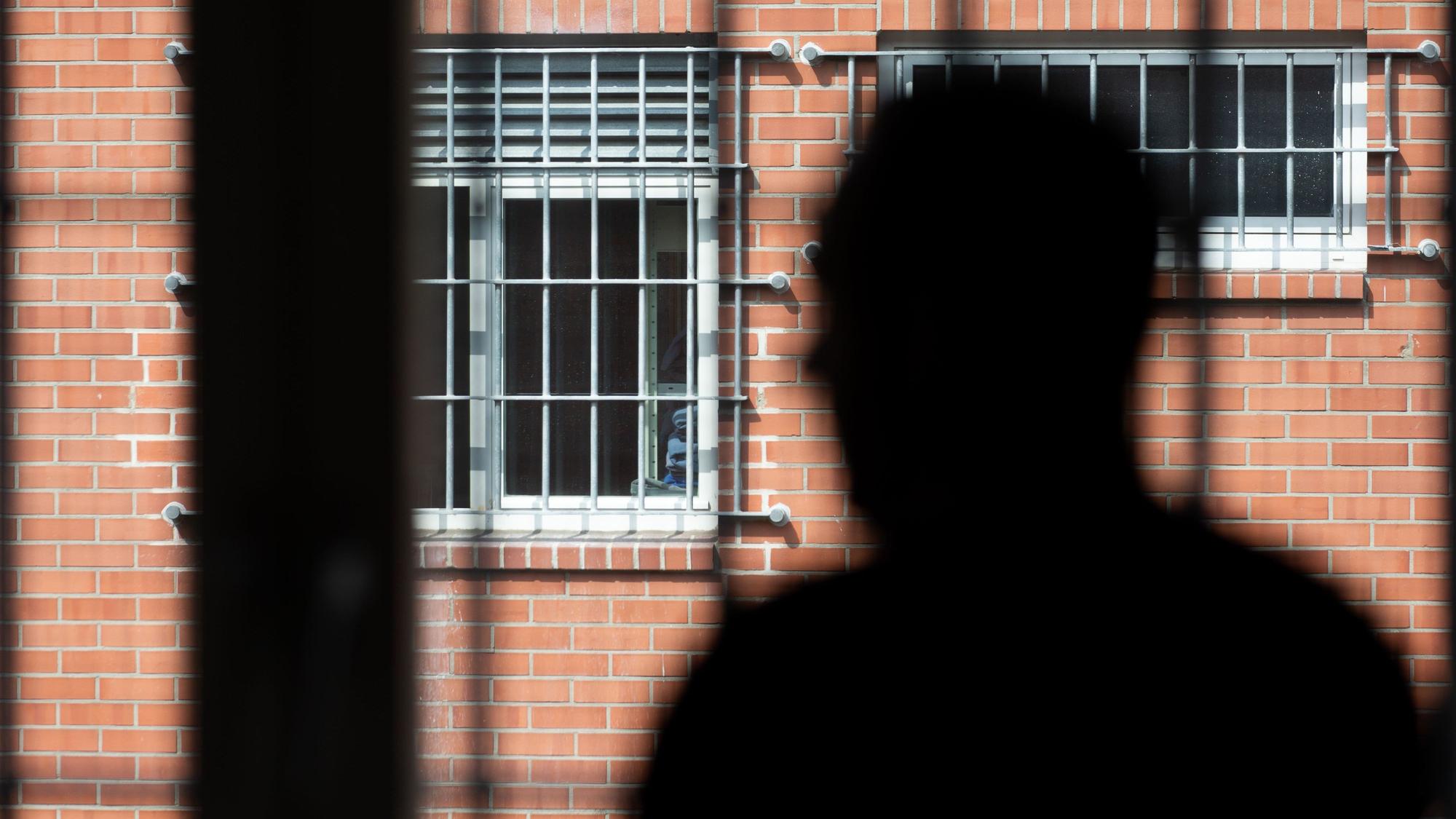 ARCHIV - 10.08.2018, Nordrhein-Westfalen, Büren: Ein Insasse steht vor einem vergitterten Fenster in der Unterbringungseinrichtung für Ausreisepflichtige in Büren.